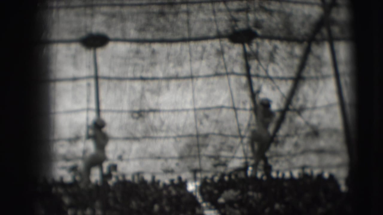 Two circus performers descend ropes inside a tent above a crowd.