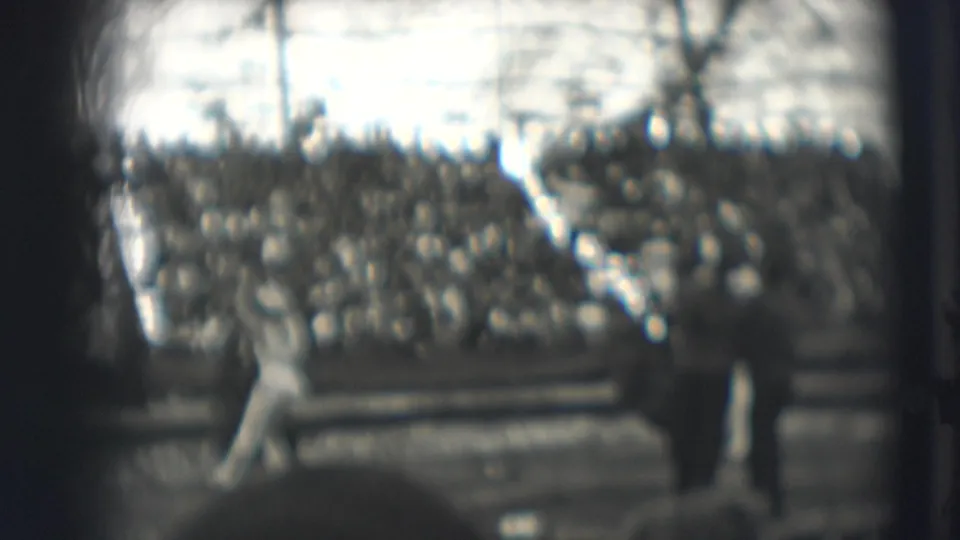 A performer remains partly visible in the tent interior while spectators sit below, framed by dark edges and soft 8mm focus.