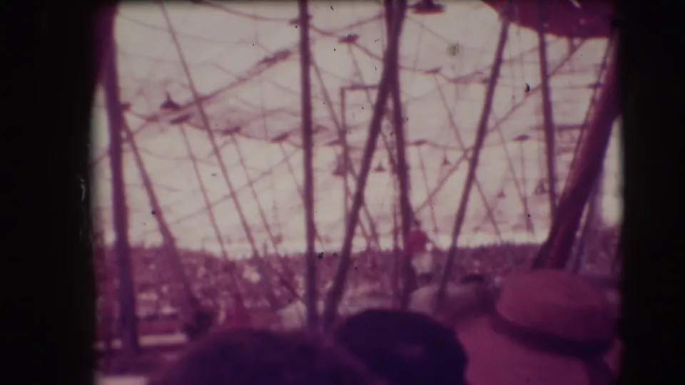 Purple-tinted 1948 circus tent interior with poles, overhead lines, and spectators below the frame line.