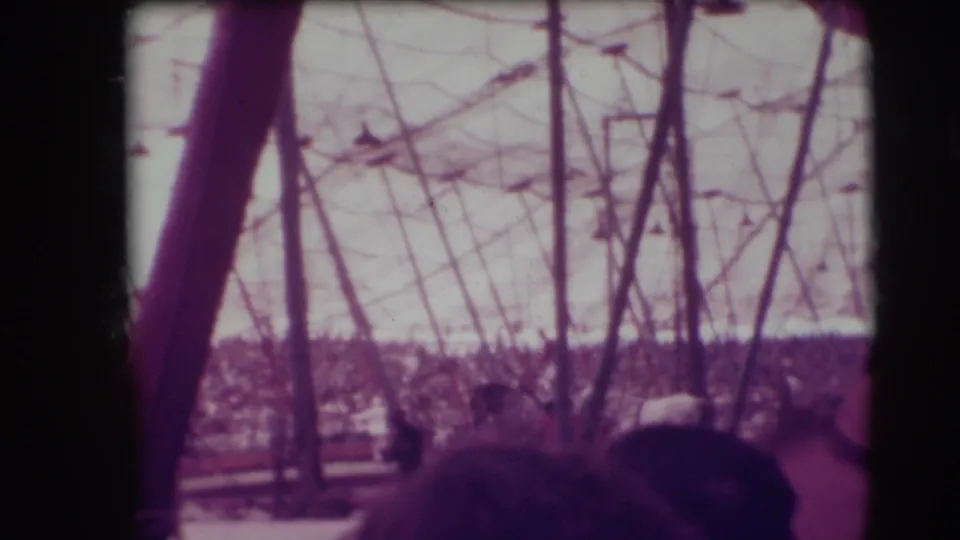 Handheld 8mm view inside the 1948 Sarasota circus tent, partially blocked by a pole and nearby audience members.
