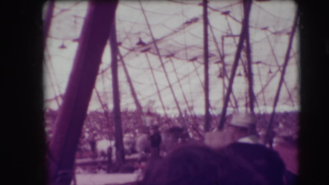 Horse and rider move across a circus ring behind foreground audience heads and tent supports.
