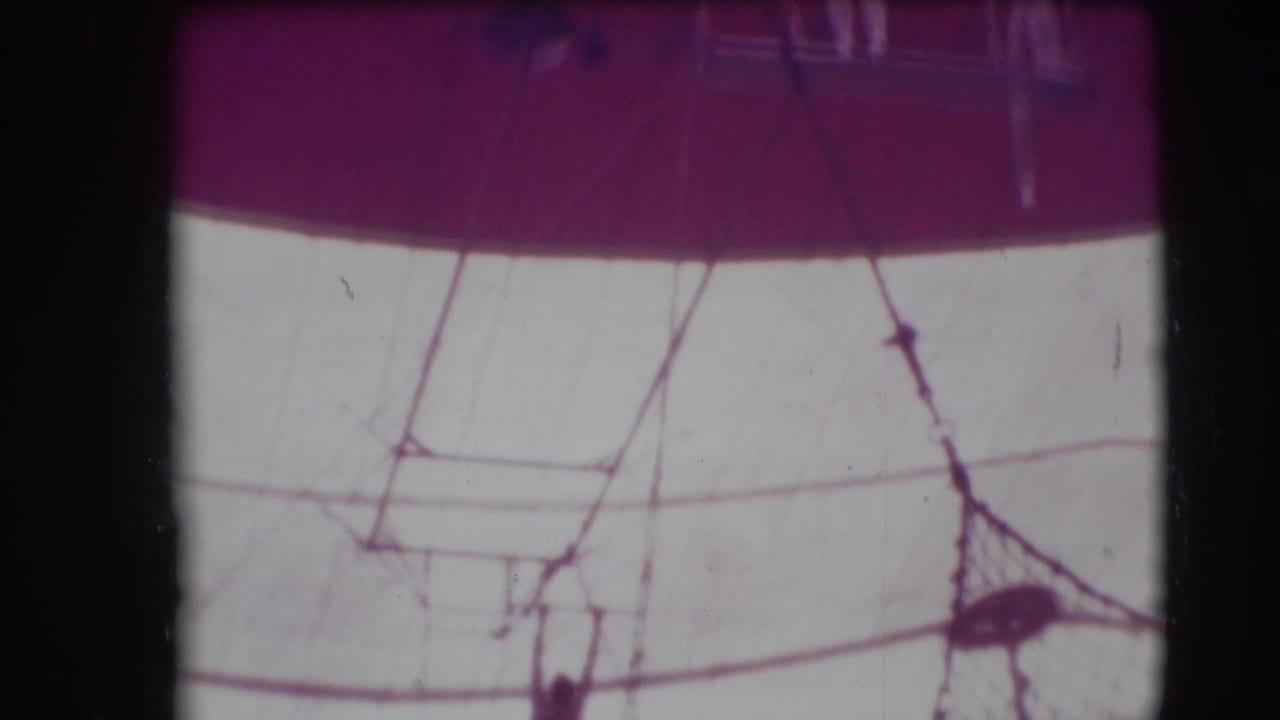 1948 Sarasota circus home-movie frame showing tent fabric, suspended rigging, and a trapeze setup before the aerial action.