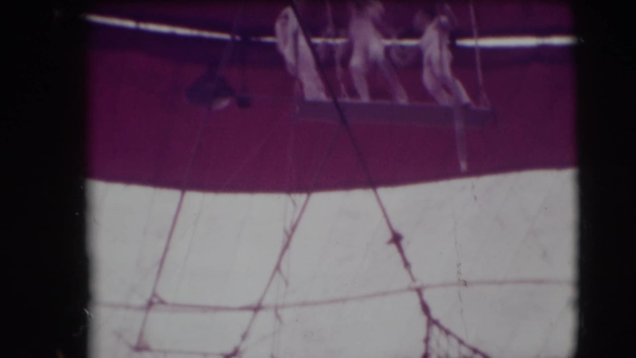 Three trapeze artists on a suspended platform near the top of a circus tent.