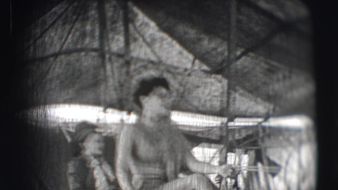 Woman riding a horse inside a circus tent with rails and equipment nearby.