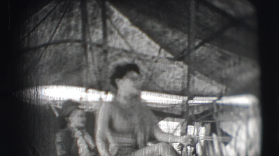 1948 Sarasota circus home-movie frame showing a woman on horseback inside a canvas tent with rails and equipment in the background.