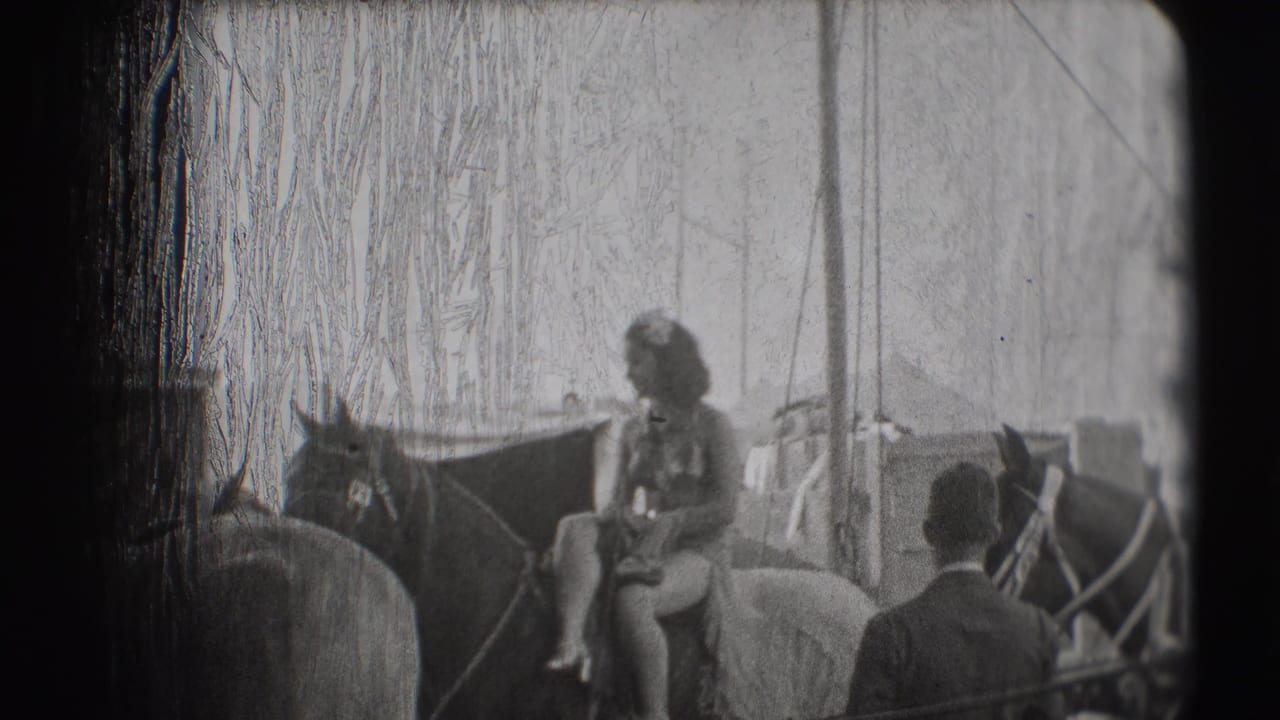 Woman seated on a horse under a circus tent with men and another horse nearby.