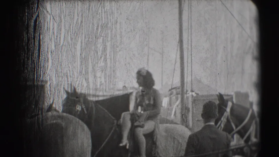 1948 Sarasota circus footage shows a woman in a flounced dress seated on a horse under tent rigging with handlers nearby.