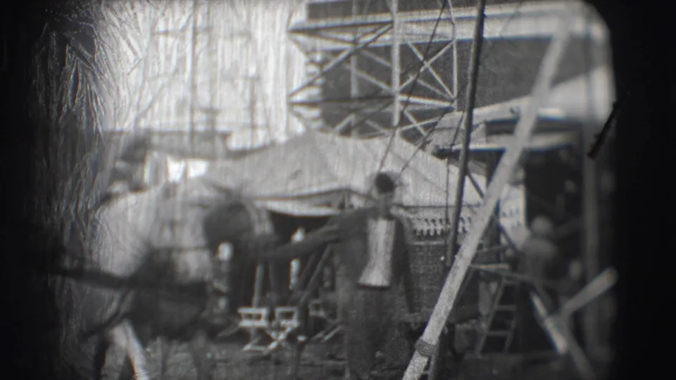 Blurred 8mm frame of people and horses moving through a busy circus area with tents, railing, and scaffold-like supports.