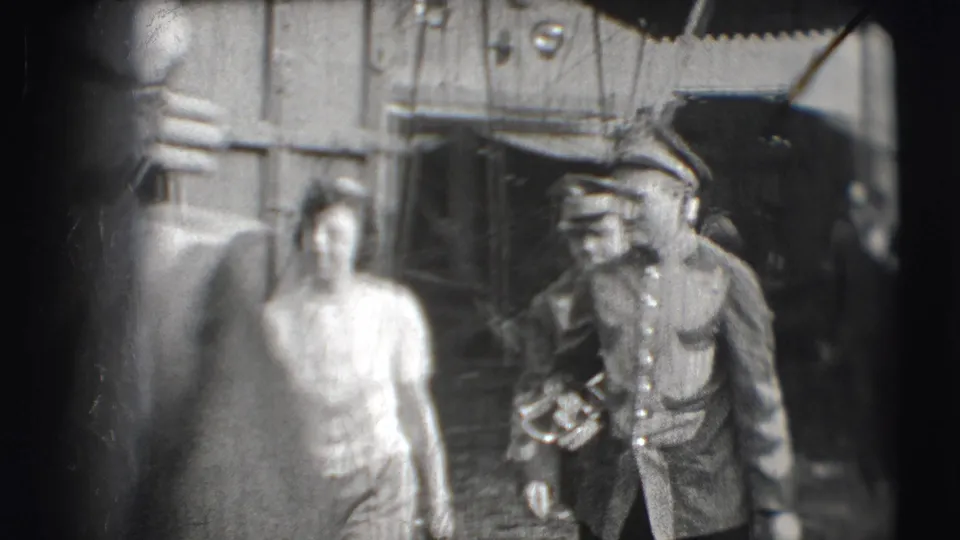In 1948 Sarasota circus footage, a uniformed musician carries a brass instrument beside a woman near a wooden circus wagon.