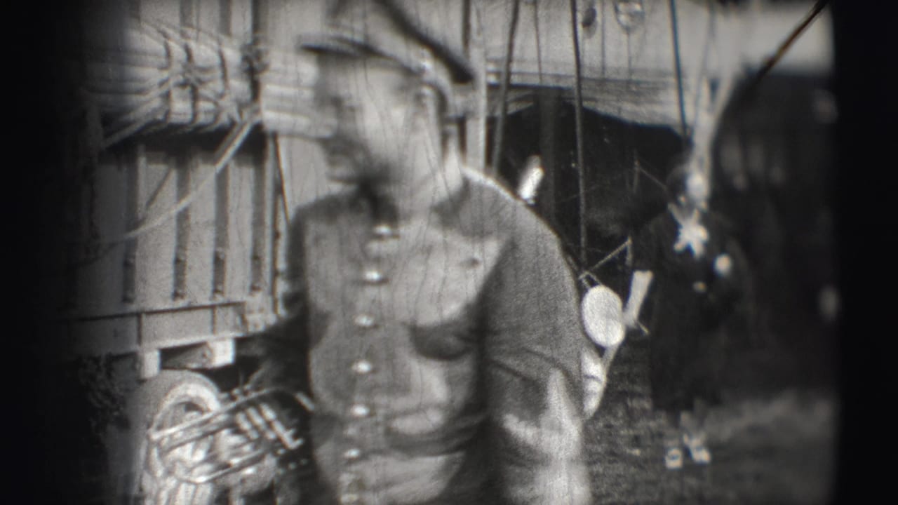 Uniformed man with brass instrument walking past circus wagon and rigging.