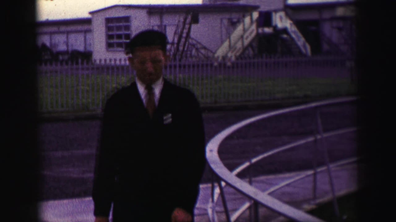 Uniformed man in a beret walking beside railings at a base compound.