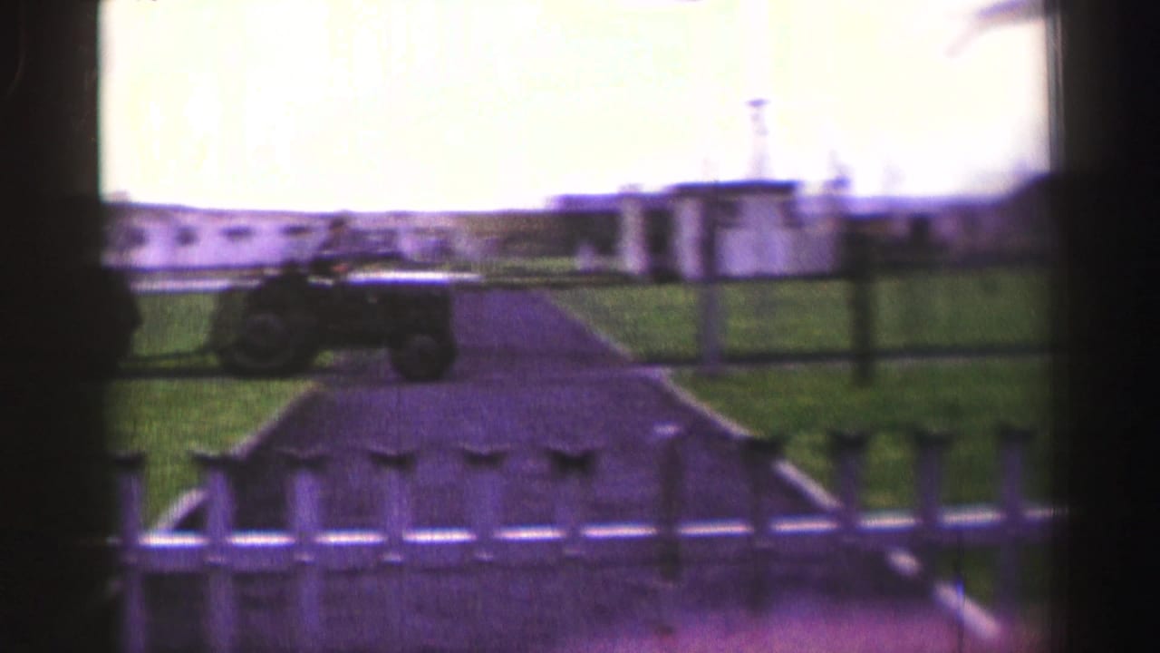 Small tractor crossing a grassy area inside a fenced compound.