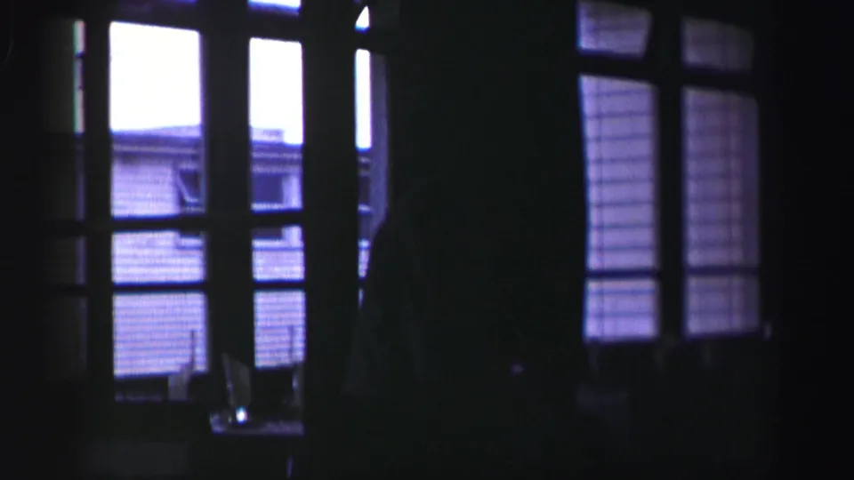 1952 United Kingdom home-movie frame showing a dark interior, window grid, and partially visible silhouetted person against bright outdoor light.