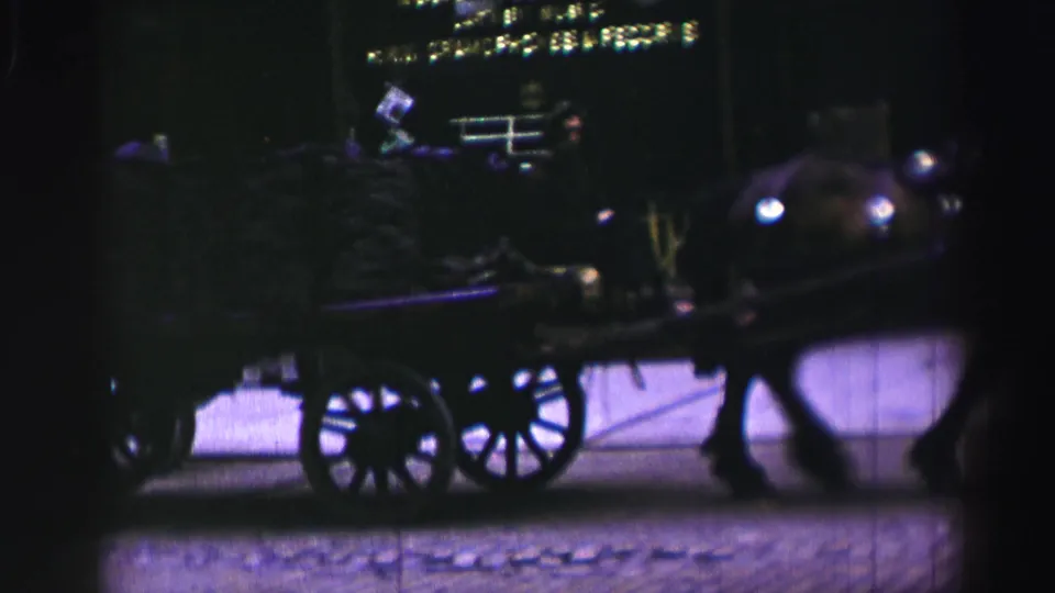 The 1952 8mm footage shows the horse and cart in soft focus, with a silhouetted rider and dark city frontage behind.
