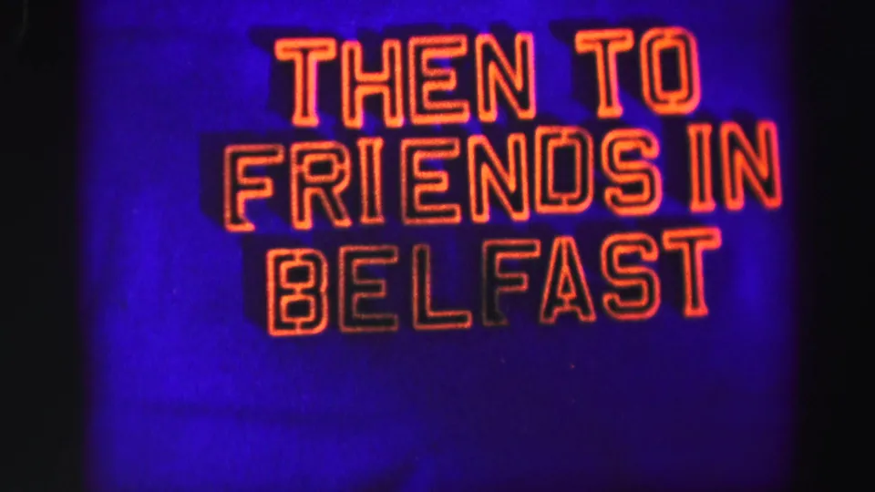 Close 8mm view of the THEN TO FRIENDS IN BELFAST sign, with cropped red-orange lettering and visible dark frame-edge shadow.