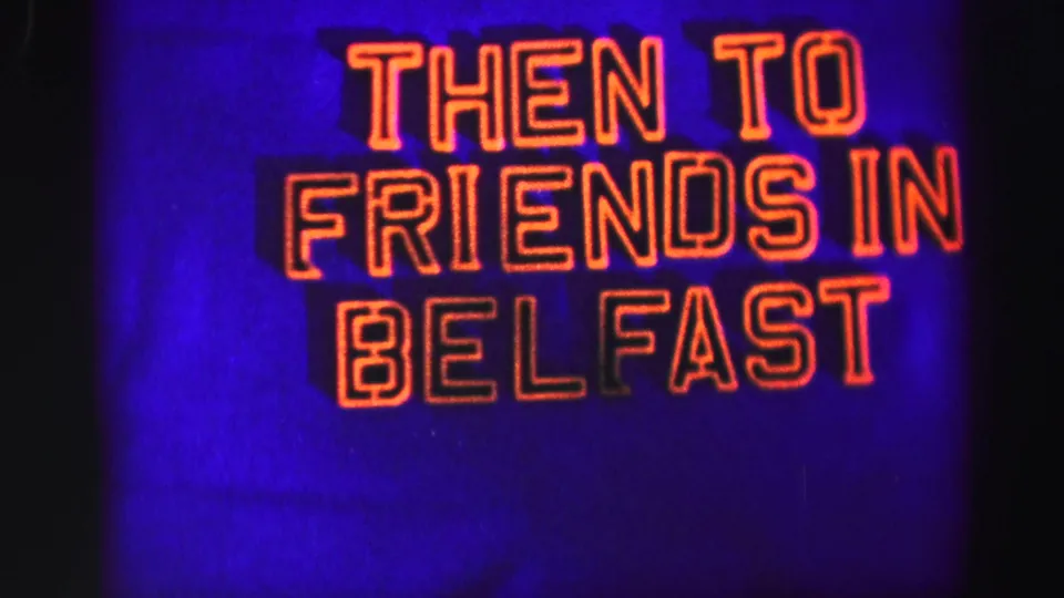 Final frame centers the glowing THEN TO FRIENDS IN BELFAST sign, with soft focus, grain, and blue-purple color shift.