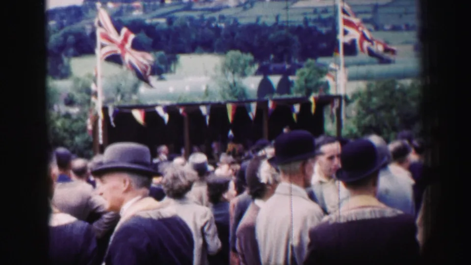 Crowd members in period clothing face a decorated rural stall with Union Jack flags in 1952 United Kingdom footage.