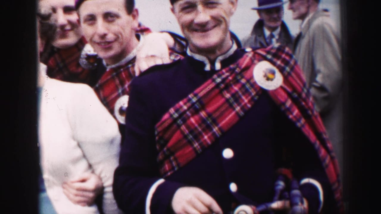 1952 United Kingdom home-movie frame of smiling uniformed bagpipers in tartan sashes standing among adults at a public gathering.