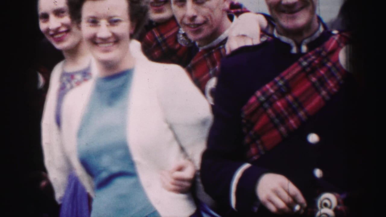 Two women stand beside men in tartan uniform, with a bagpiper partly visible at right.