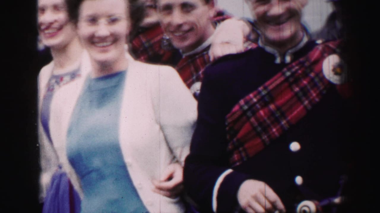 1952 United Kingdom home-movie frame of smiling adults gathered closely, with men in tartan garments beside women in pale cardigans.
