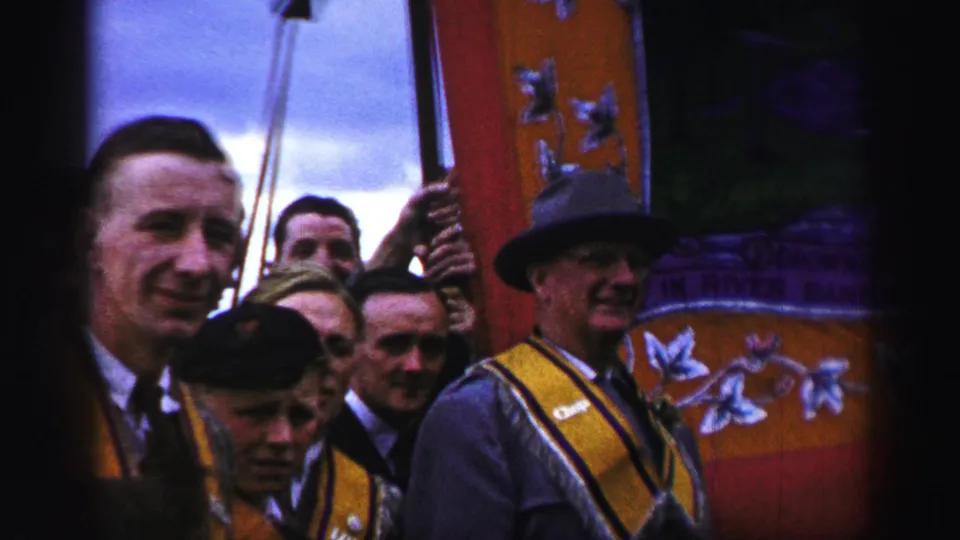 1952 United Kingdom frame of men in formal dress and sashes gathered around a decorated banner, including one man in a tall hat.
