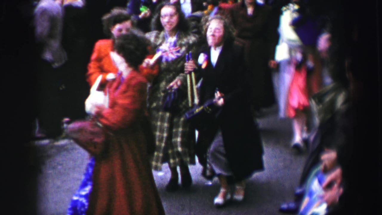 A woman in a red coat turns near women in plaid and dark coats in a crowd.