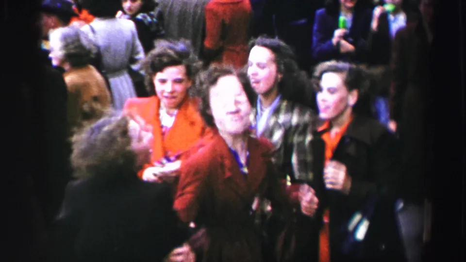 1952 United Kingdom street celebration frame with women in colorful coats laughing and moving together among bystanders.