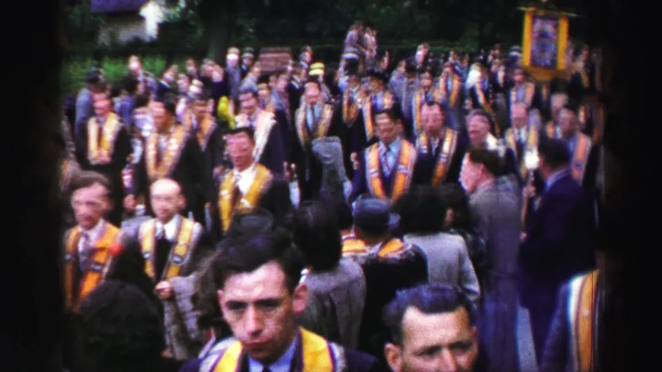 1950s home-movie frame with soft focus and motion blur as sashed participants pass close to the camera.