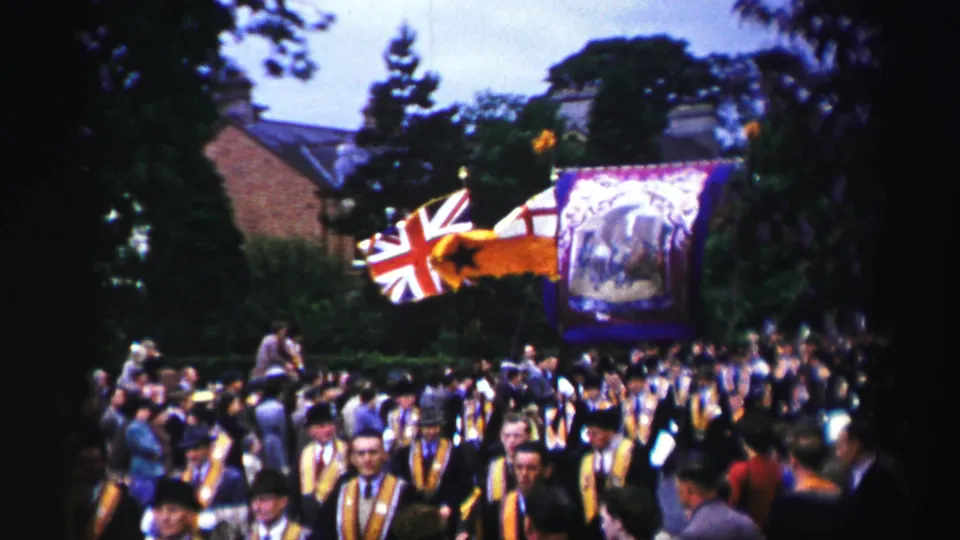 Union Jack flags and a large purple banner are visible over a dense 1952 United Kingdom parade crowd filmed from the side.