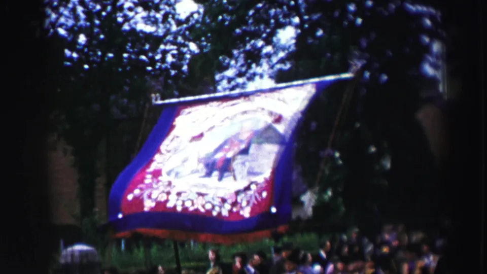 The same large decorated parade banner is seen from below, carried above spectators beneath trees in 1952 United Kingdom footage.