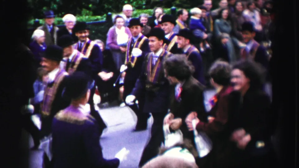 1952 United Kingdom home-movie view of formal parade participants in sashes passing a dense sidewalk audience.