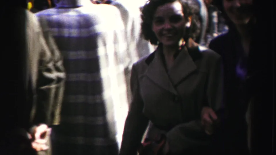 Close home-movie frame from the 1952 United Kingdom parade showing a woman in a light coat near the camera and blurred passersby behind her.