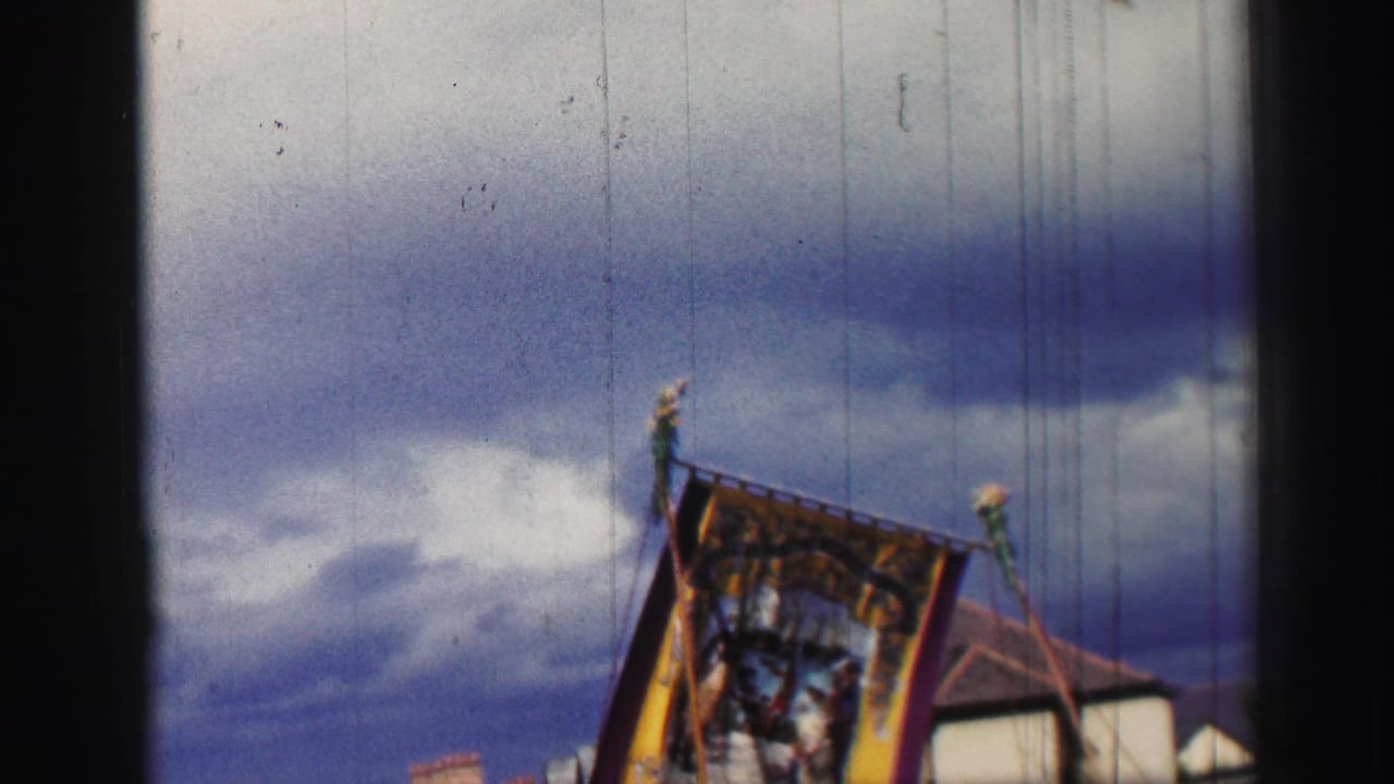 A painted religious banner appears above rooftops during the United Kingdom parade, framed by dramatic cloud cover and film scratches.