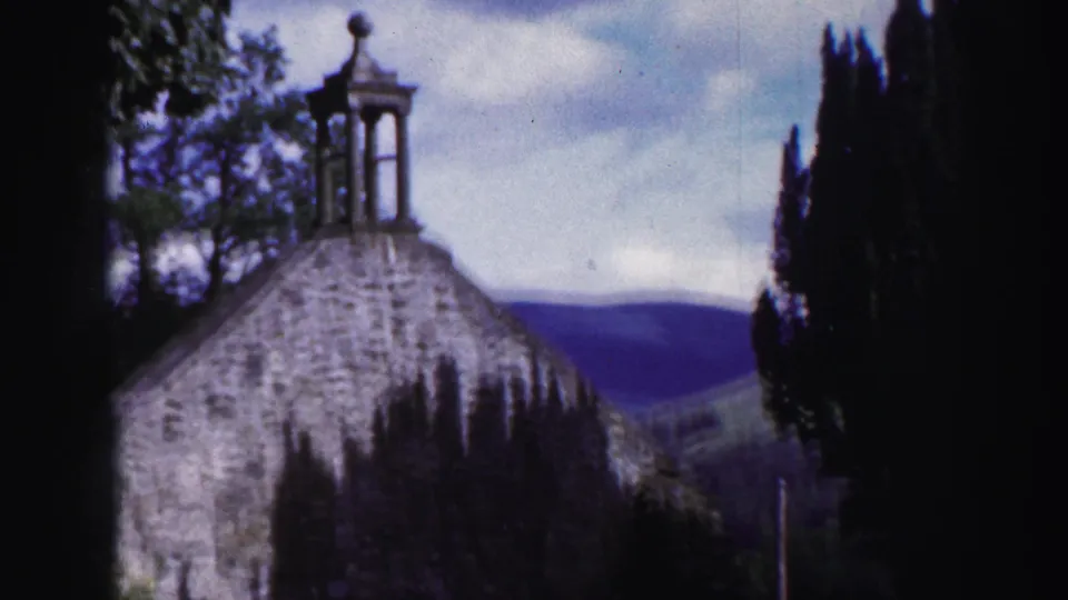 The church exterior remains framed from a nearby viewpoint, with the small bell tower silhouetted above the stone roof and hills beyond.