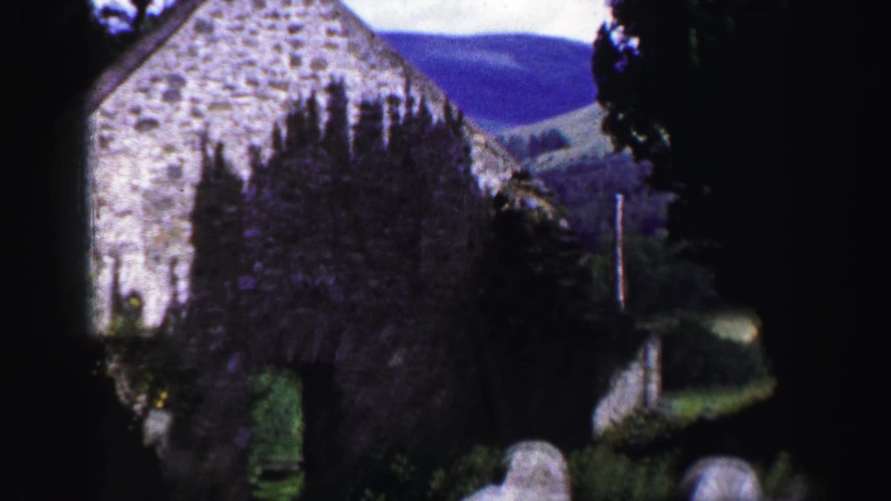 1952 United Kingdom 8mm frame showing a weathered stone building seen through trees, with hillside visible beyond.