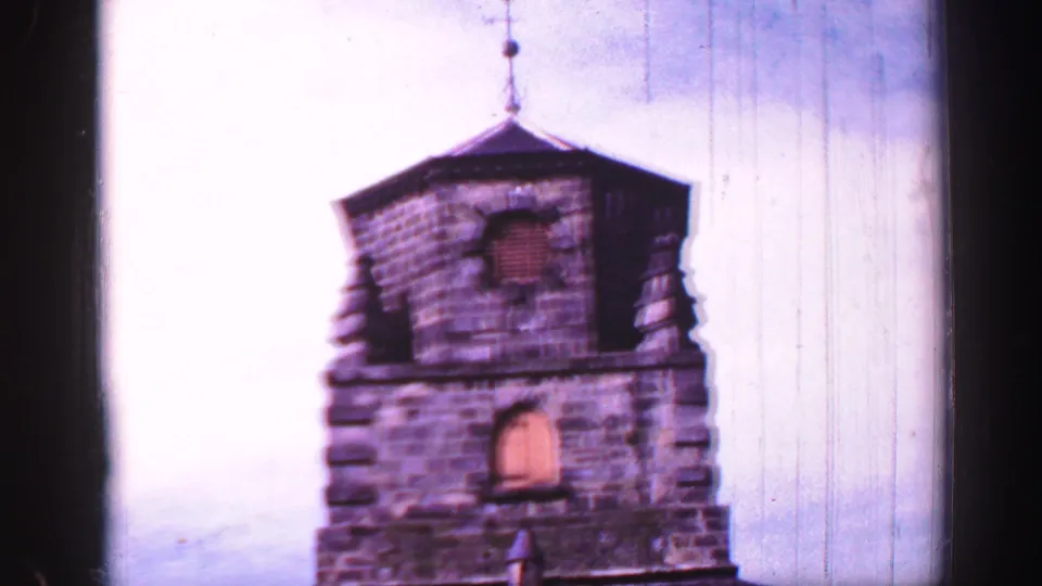 1952 United Kingdom home-movie frame showing a weathered stone church tower in Burntisland, softly focused against a pale sky.