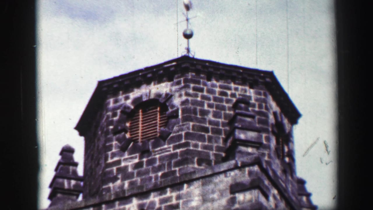 1952 United Kingdom 8mm frame looking up at a weathered stone tower with a louvered opening and weather vane.