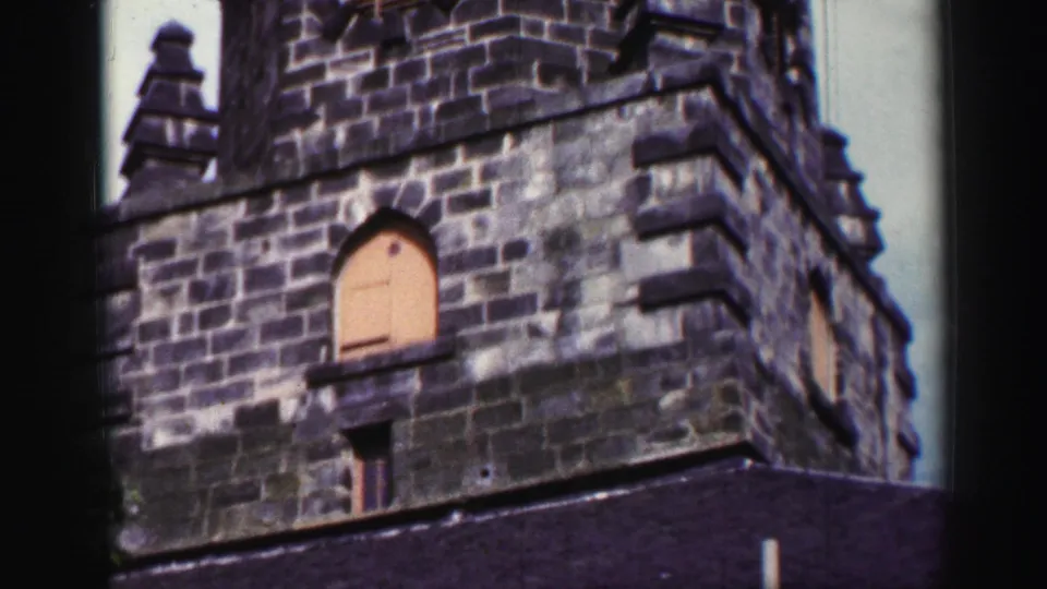 1952 United Kingdom 8mm frame showing the tower from below, with shuttered openings, roof edge and a weather vane above.