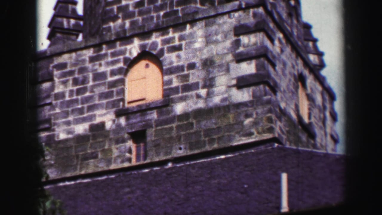 1952 United Kingdom 8mm frame showing the upper stone facade of an older building with arched openings and dark roof edge.