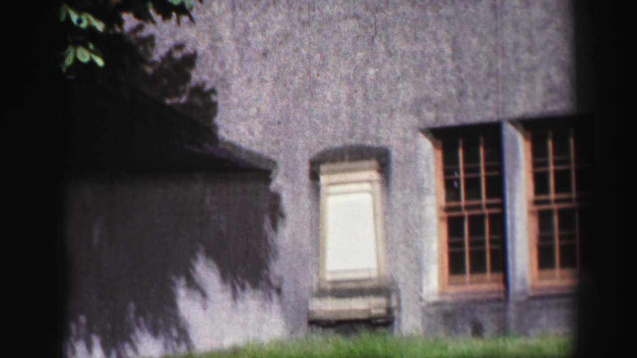 1952 United Kingdom home-movie view of Inchcolm Abbey exterior with weathered stone walls, windows, grass, and heavy edge shadow.