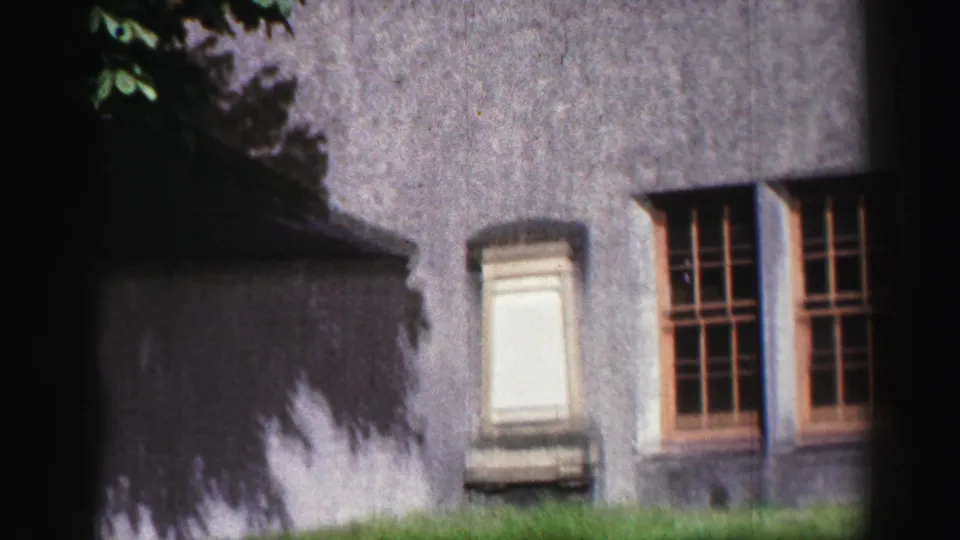 1952 United Kingdom home-movie view of Inchcolm Abbey exterior with weathered stone walls, windows, grass, and heavy edge shadow.