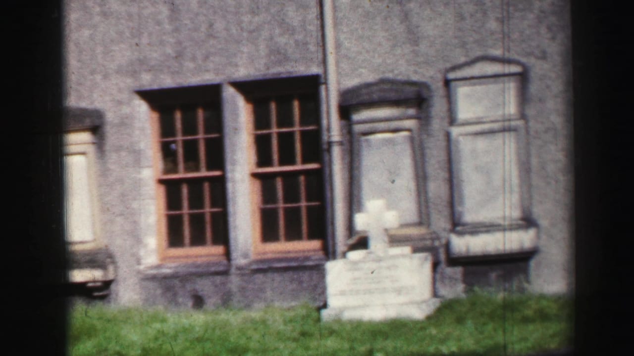 1952 United Kingdom footage showing Inchcolm Abbey exterior with tall windows, grass, and a small gravestone or marker near the wall.