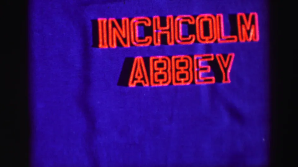 Filmed title card reading INCHCOLM ABBEY in red lettering on a saturated blue background, with visible 8mm grain and edge shadow.