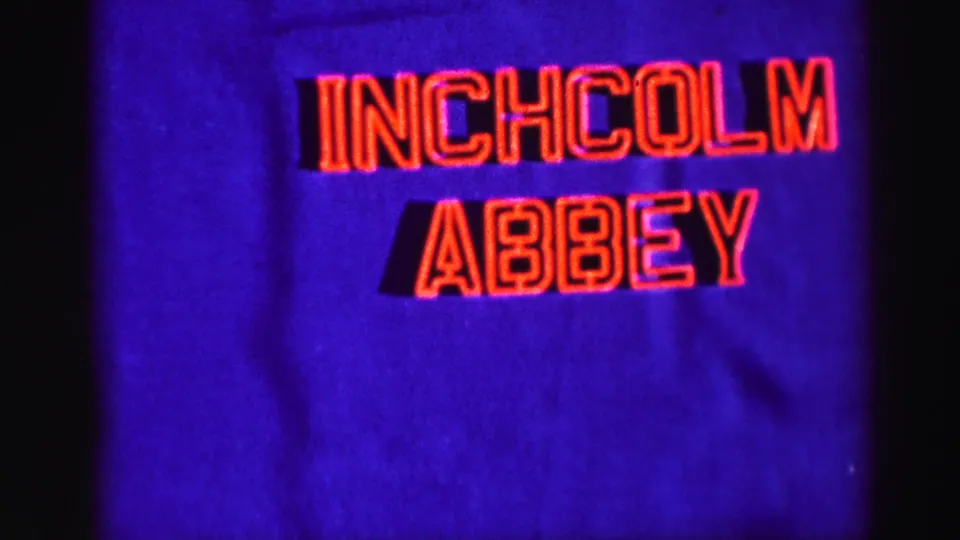 Final 1952 home-movie title frame for Inchcolm Abbey, showing red lettering on blue with dark vertical film-edge shadows.
