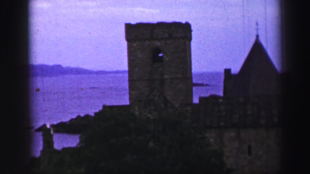 Inchcolm Abbey ruins appear in silhouette above the Firth of Forth shoreline in 8mm color footage.