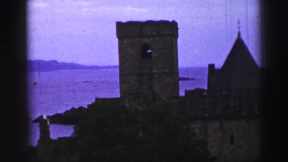 Inchcolm Abbey ruins appear in silhouette above the Firth of Forth shoreline in 8mm color footage.