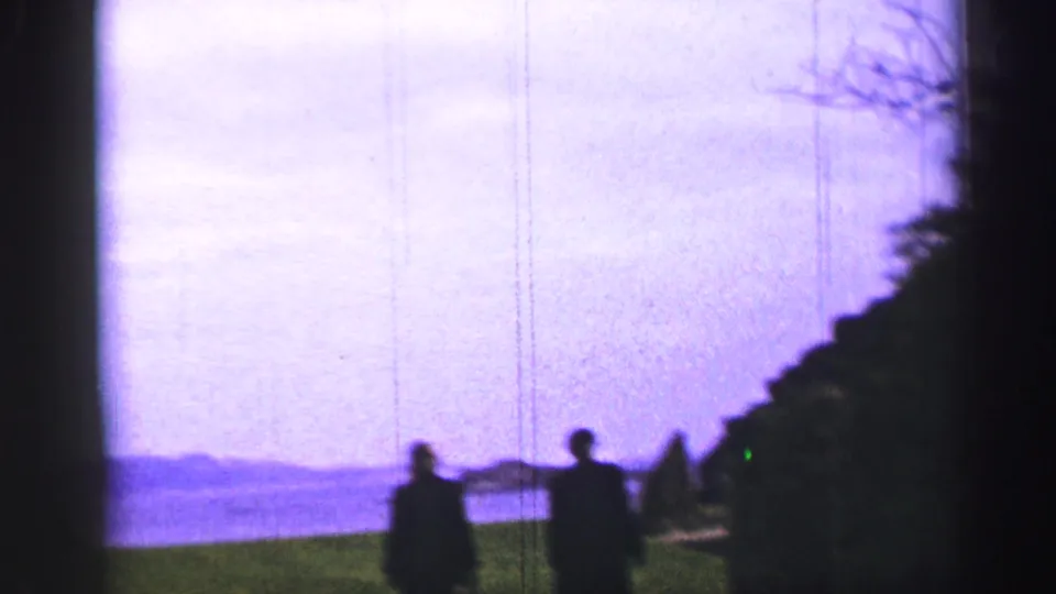 Two elderly visitors appear as dark silhouettes near the abbey grounds with water and shoreline beyond.