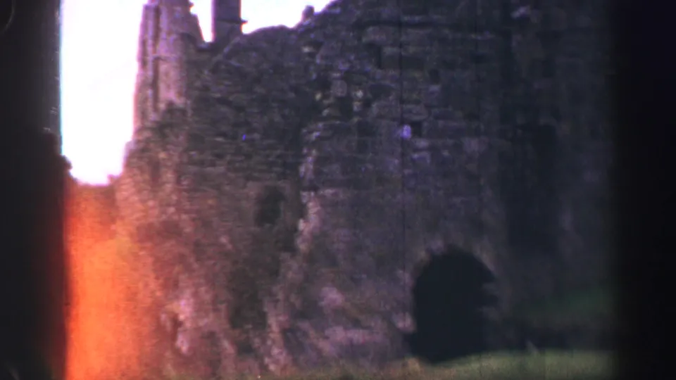 Stone castle ruins and a narrow path appear in warm light, with a partial visitor figure at the lower edge of the 1952 UK frame.