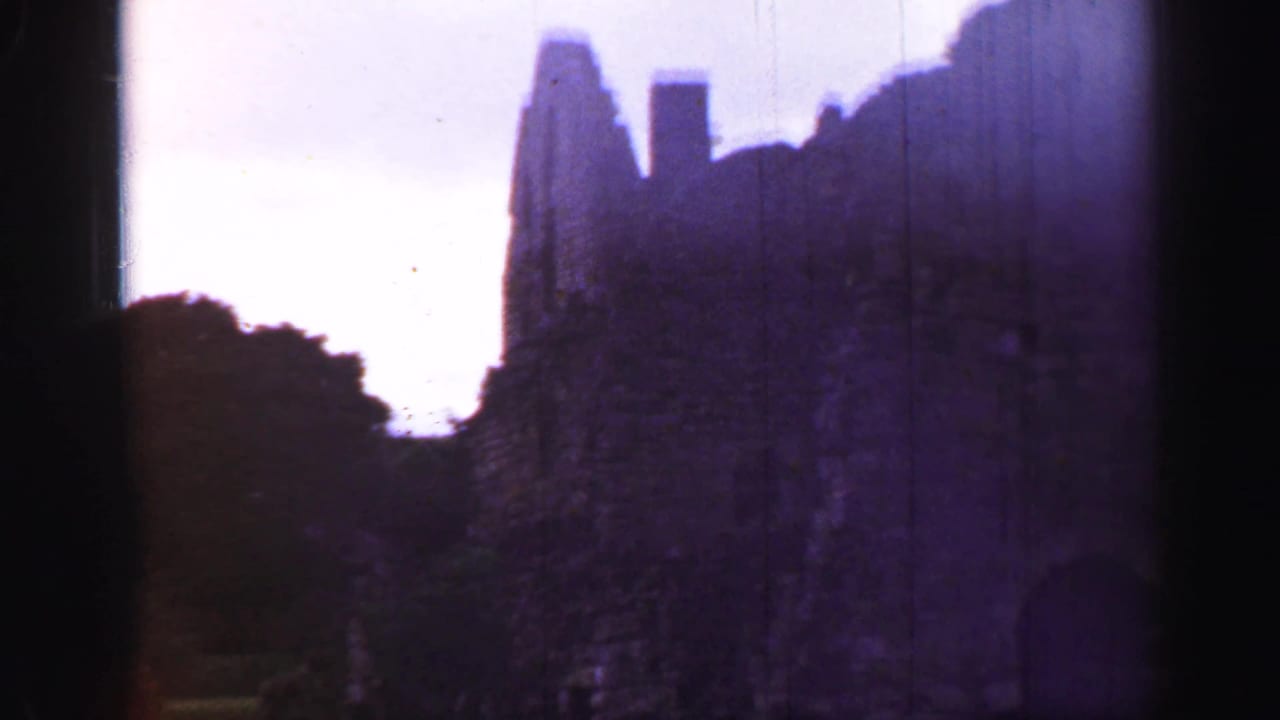 Dark-framed view of a stone ruin with trees and hills behind it.