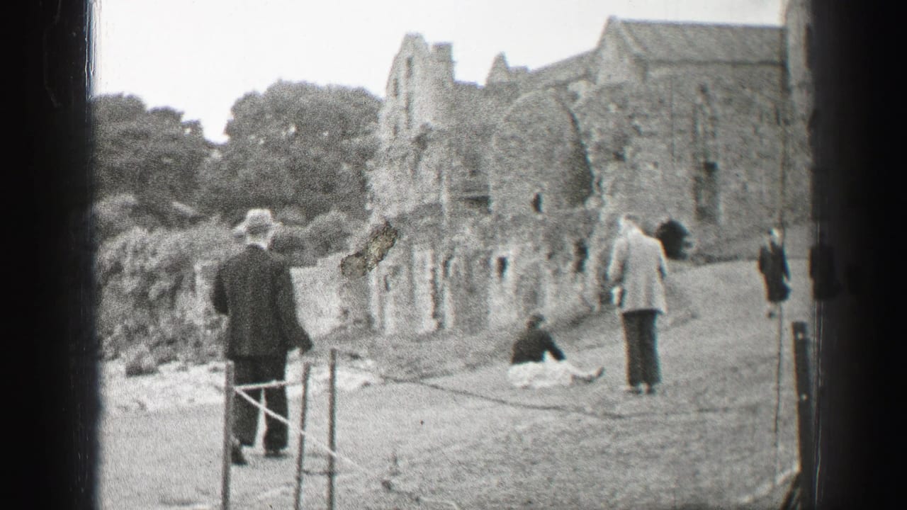 Tourists walk and stand near a weathered stone ruin on a grassy path.